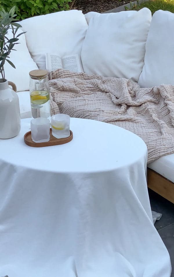 Beżowy koc muślinowy na ogrodowej sofie obok stolika z lemoniadą